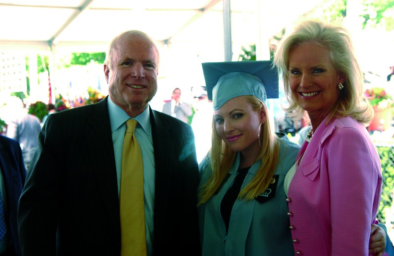 A young woman in an academic gown and mortar is flanked by her parents.