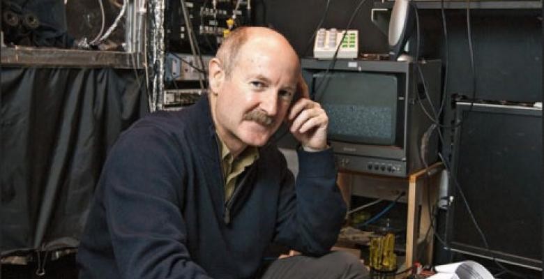 Photo courtesy of Columbia University Wearing a blue pullover with leather elbow patches, a man rests his index finger against his temple, as he sits in front of a laboratory desk filled with computer equipment