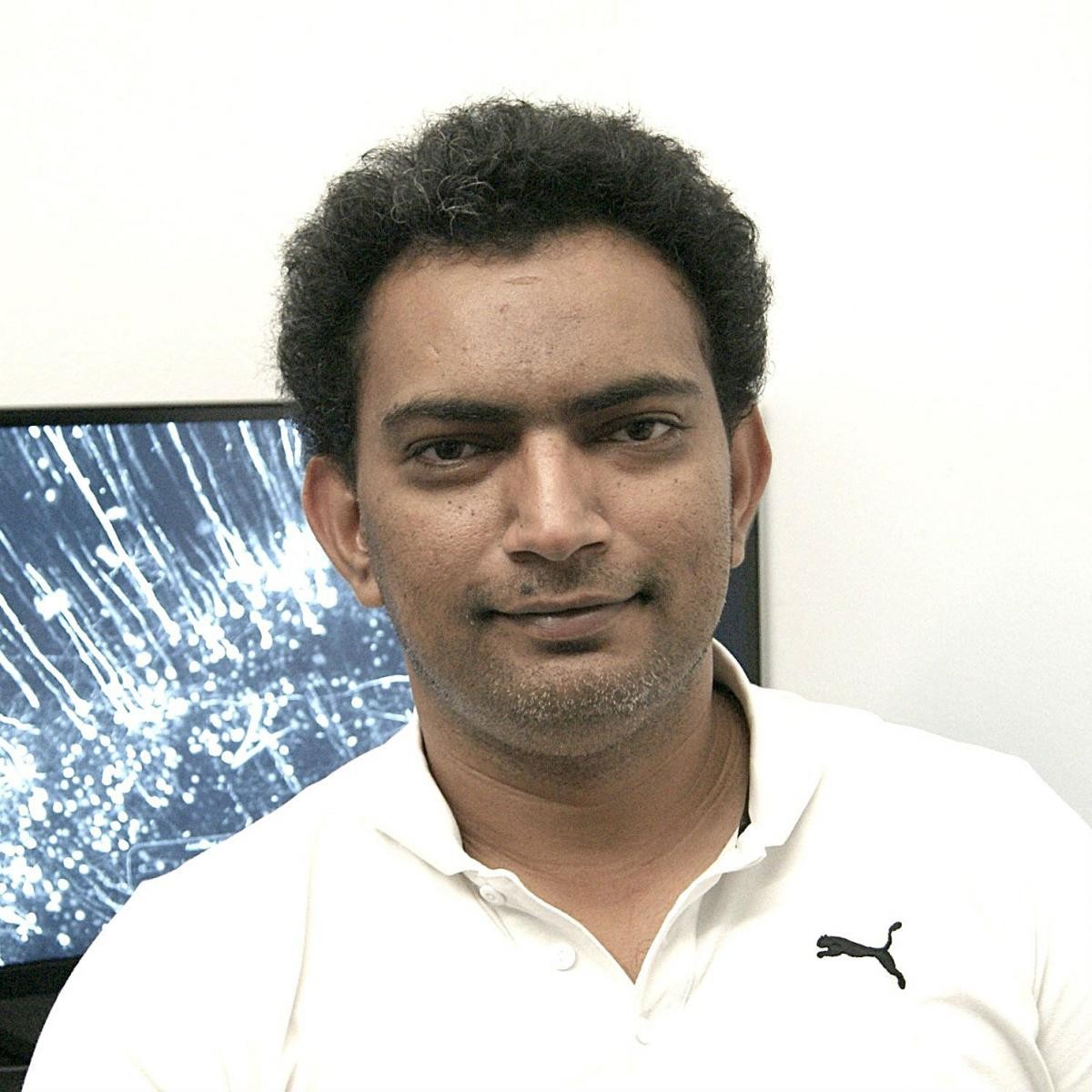 A man stands in front of a computer screen smiling into the camera.
