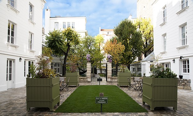 A manicured courtyard with potted trees and plants and flagstone pavers is flanked by three- and four-story limestone buildings