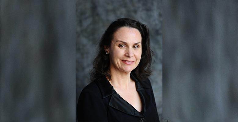 A woman, with shoulder-length hair and wearing a black dress, smiles into the camera