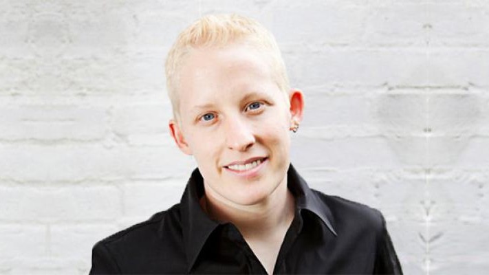 Tey Meadow, wearing a black, collared dress shirt, smiles into the camera