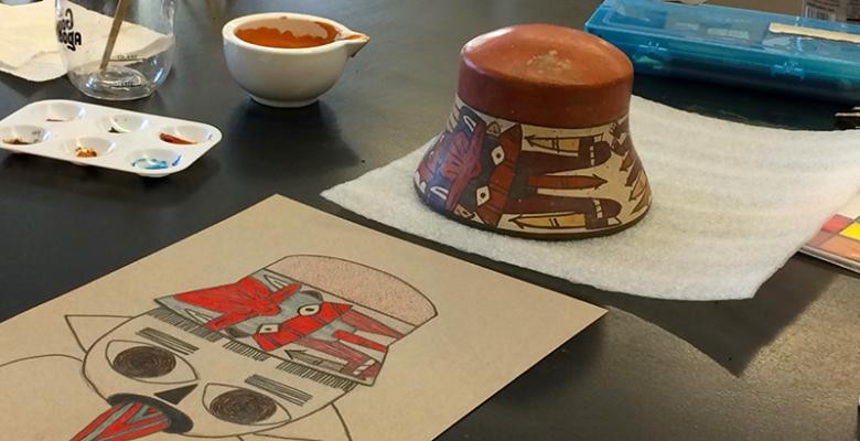 Illustration of a Nasca vessel by Jiayan Lu (MA Anthropology). Photo by Zoë Crossland A table top holds a vessel filled with paint, a palette, an earthen vase, and an illustration of the characters depicted on the vase