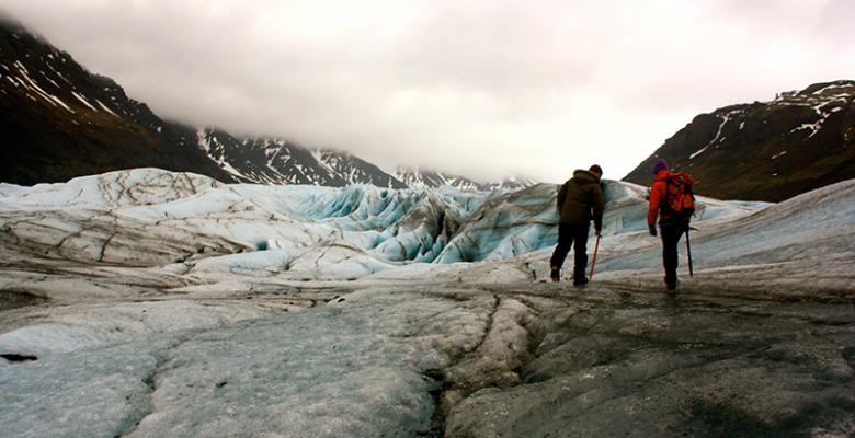 Photo by Rebecca Fowler Two people trek across the surface of a glacier, high in the clouds