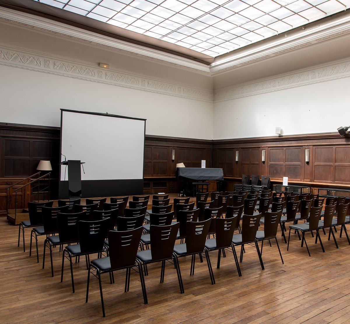 Photograph of a large room with chairs lined up in front of a screen and podium; skylight overhead