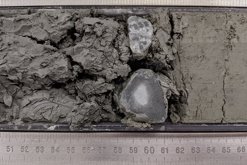 A close-up shot of dropstones coming out of sediment with a ruler underneath to measure the stones. 