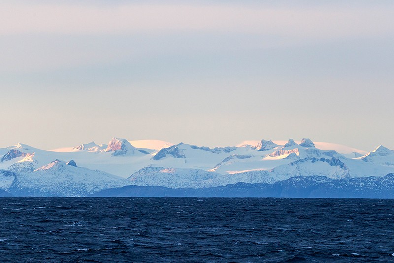 The white and blue landscape of the snowy Patagonian mountains by the ocean.