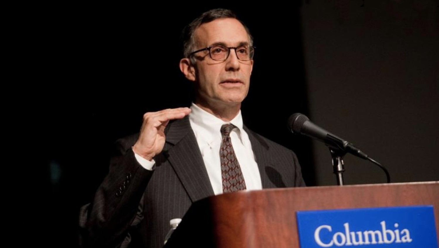 Man with glasses at podium speaking