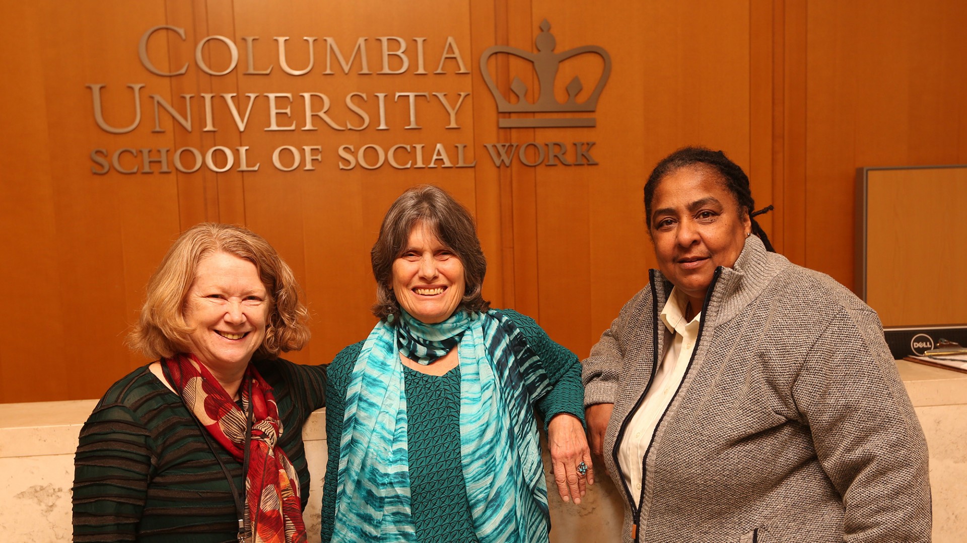 Geraldine Downey, Kathy Boudin, and Cheryl Wilkins stand in front of a marble counter with a wooden panel in the background with the words Columbia University School of Social Work on it.