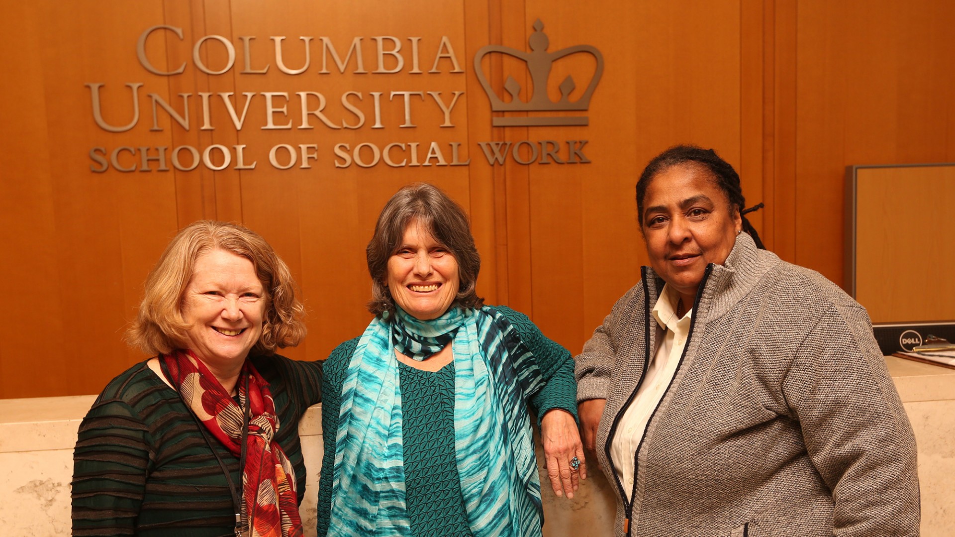 From left to right: Geraldine Downey, Kathy Boudin, and Cheryl Wilkins. Photo by Bruce Gilbert Geraldine Downey, Kathy Boudin, and Cheryl Wilkins stand in front of a marble counter with a wooden panel in the background with the words Columbia University School of Social Work on it.