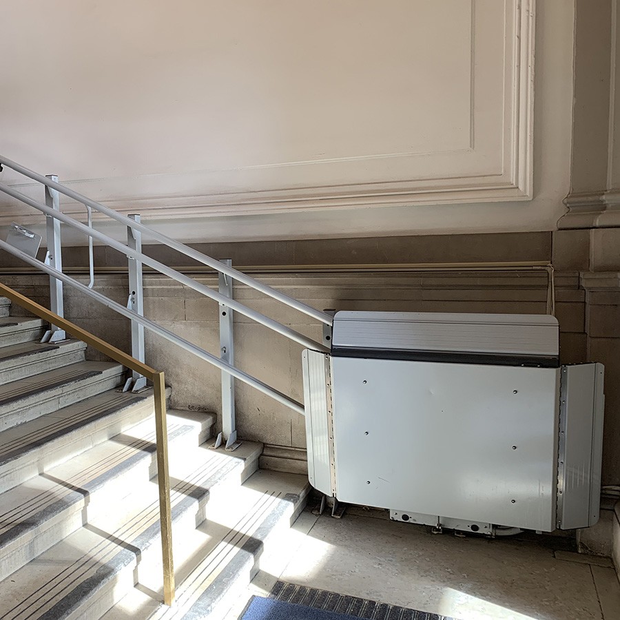 A wheelchair lift sits at the bottom of a staircase in Lewisohn Hall.