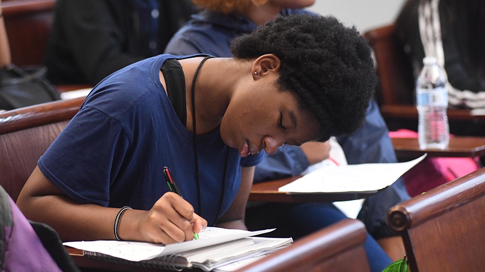 Teenage girl at a classroom desk writing in a notebook