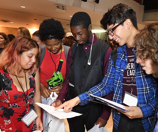 Since 1965, the Center's goal has remained constant: to increase high school graduation and college enrollment for students from neighboring low-income communities. According to kecia hayes, Executive Director of Double Discovery Center, "This year, our seniors collectively earned admission to over 100 institutions of higher education with more than $3 million in grants and scholarships." Five teenagers in an auditorium looking at a brochure
