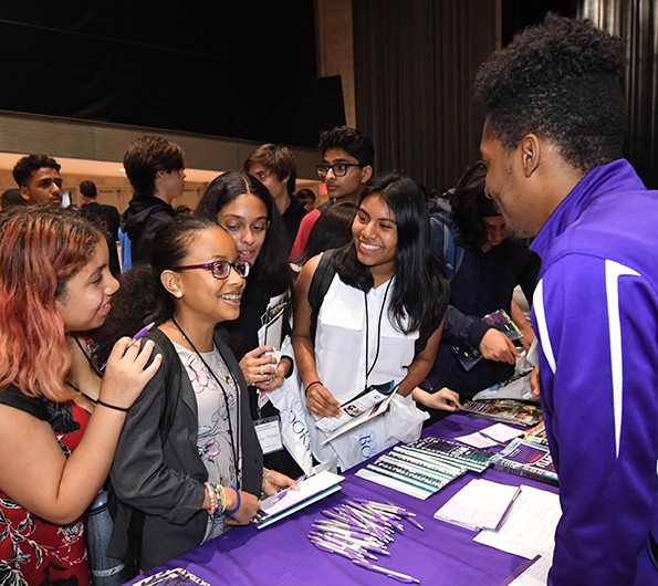 Four teenage girls talking to a young man behind a table at a college fair