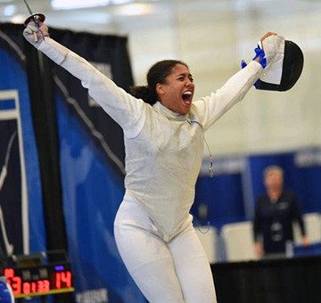 Iman Blow, still in uniform and with a sword in hand, celebrates a fencing victory.