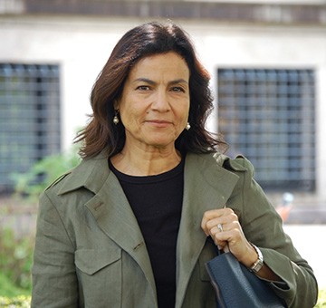 Rachel Ticotin wearing a forest green jacket and holds a black purse.