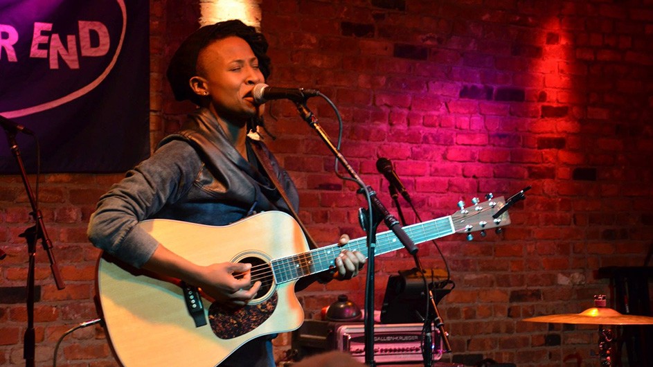 Sondra Woodruff performing on an acoustic guitar and microphone in an intimate club.