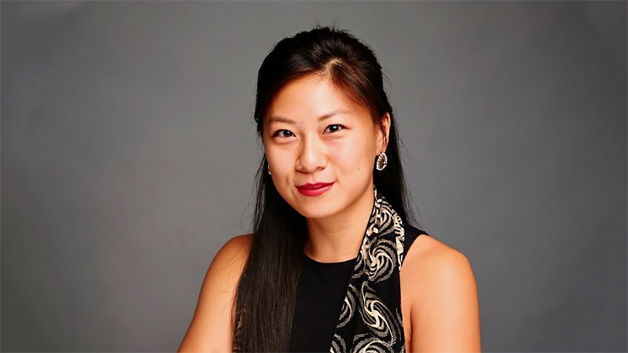 Sun-Ming Jessica Pan in a black dress and gray scarf, stands in front of a gray backdrop.