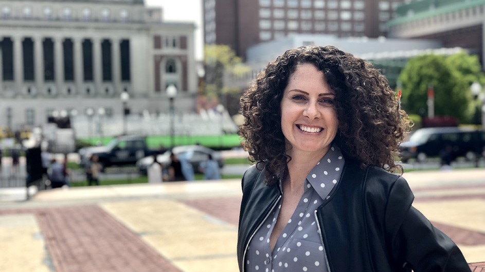 Tara Heidger in a polka dot blouse and black blazer on College Walk with Butler Library in the background.