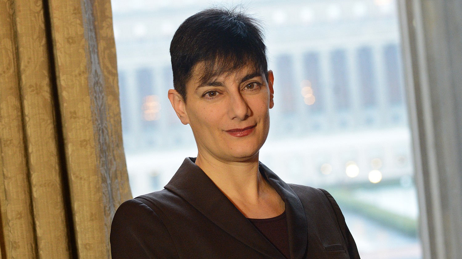 Woman with short dark hair looking at camera with window in the background