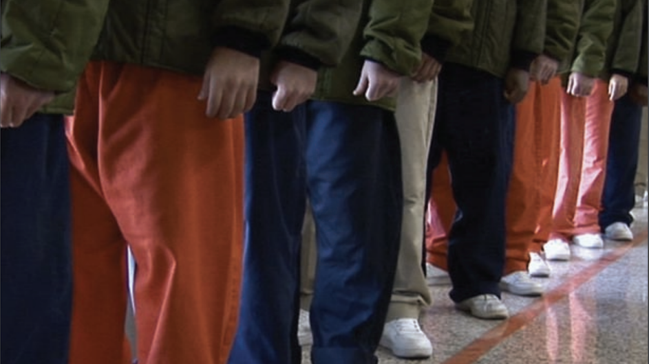 Image of people's legs in blue and orange pants and they are wearing khaki colored jackets, but can't see above elbow