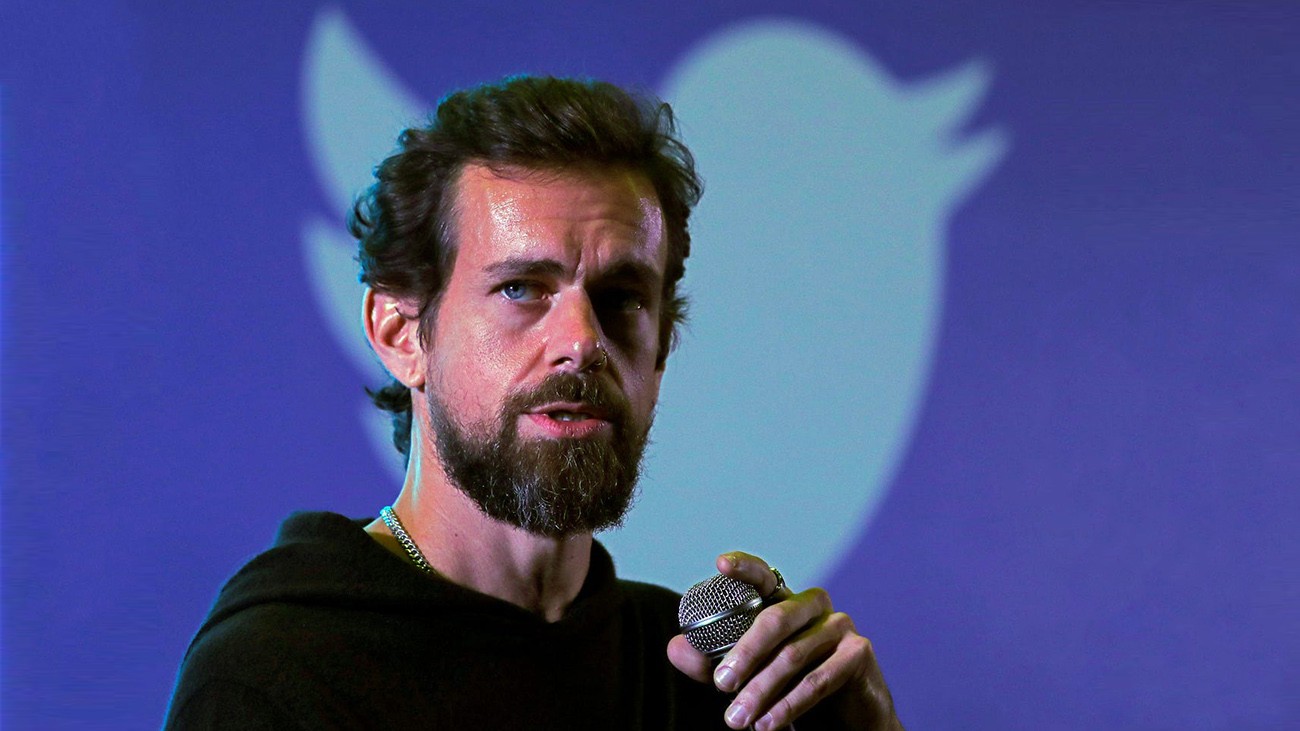 Man with beard standing in front of an image of the Twitter bird logo.