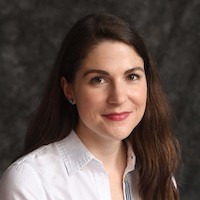 A headshot of a woman with long brown hair who is wearing a white buttoned down collared shirt