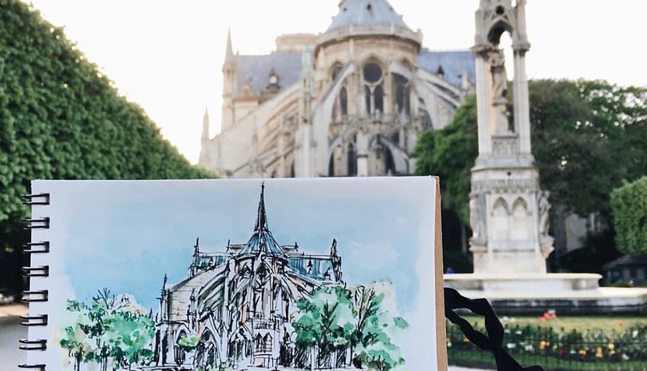Pearada Unahalekhaka holds up her sketchbook with a drawing of Notre Dame in front of the building itself.