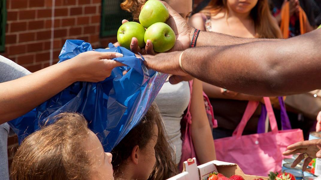 Someone putting three green apples in a blue bag for someone else.