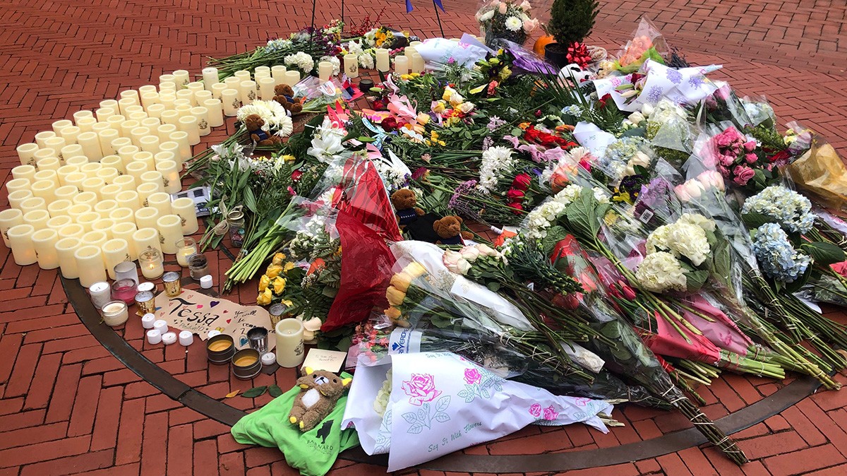 A pile of flowers, candles and teddy bears on the red brick walkway of Barnard College’s courtyard.