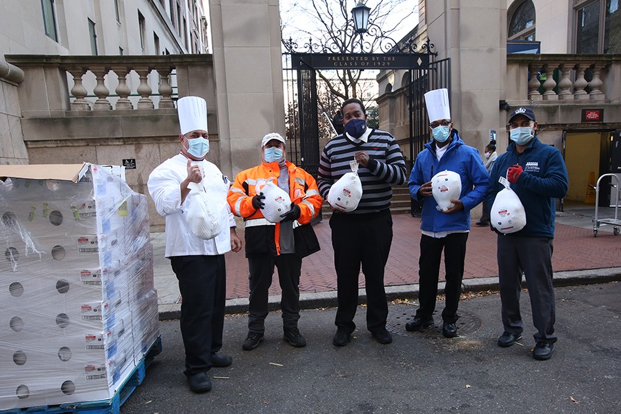 Five people stand in front of Columbia University's gates holding turkeys to give away.