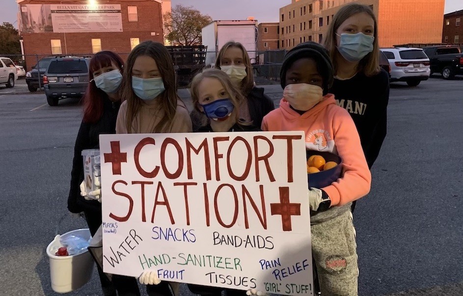 A photo of six girls with masks holding a sign saying "Comfort Station"