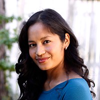 Headshot of a medium-skinned woman with long dark hair and a medium blue top