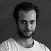 Black and white headshot of a light-skinned man with short dark hair, a dark mustache and beard, in a white t-shirt.