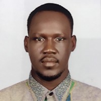 Headshot of dark-skinned man with short, dark hair, a dark beard and mustache, in a light brown shirt.