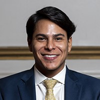 Man with short, dark hair, in a dark blue suit and light yellow tie.