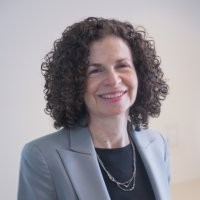 Jessica Justman with short curly hair, wearing a gray blazer and black blouse.