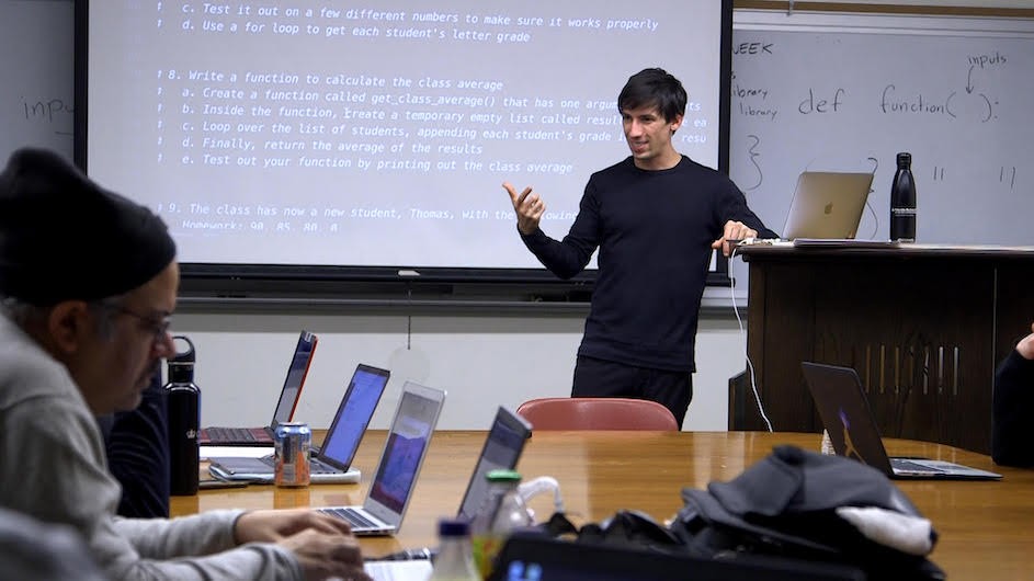 Justice Through Code instructor, Mattan Griffel, with students in class, in February 2020, before the global pandemic curtailed in-person instruction. A man in front a white board teaching students in a classroom