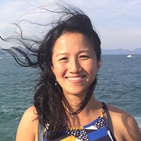 Photo of a medium-skinned woman with dark hair blowing in the wind against an ocean backdrop