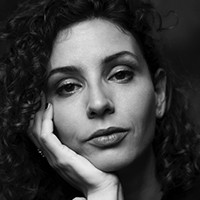 Headshot of a light-skinned woman with dark curly hair, cupping her face with her hand