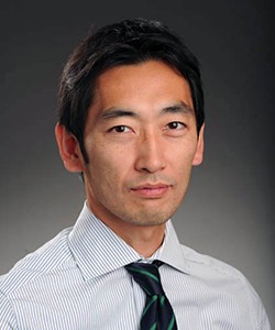 Headshot of Shunichi Nakagawa, a young man with short, dark hair,  in a light striped shirt and dark blue striped  tie