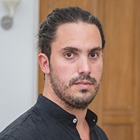 headshot of a light-skinned man with dark hair, a short mustache and beard, in a black collared shirt