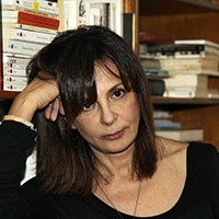 Headshot of a light-skinned woman with dark, medium-length hair in a black top, against a bookshelf backdrop