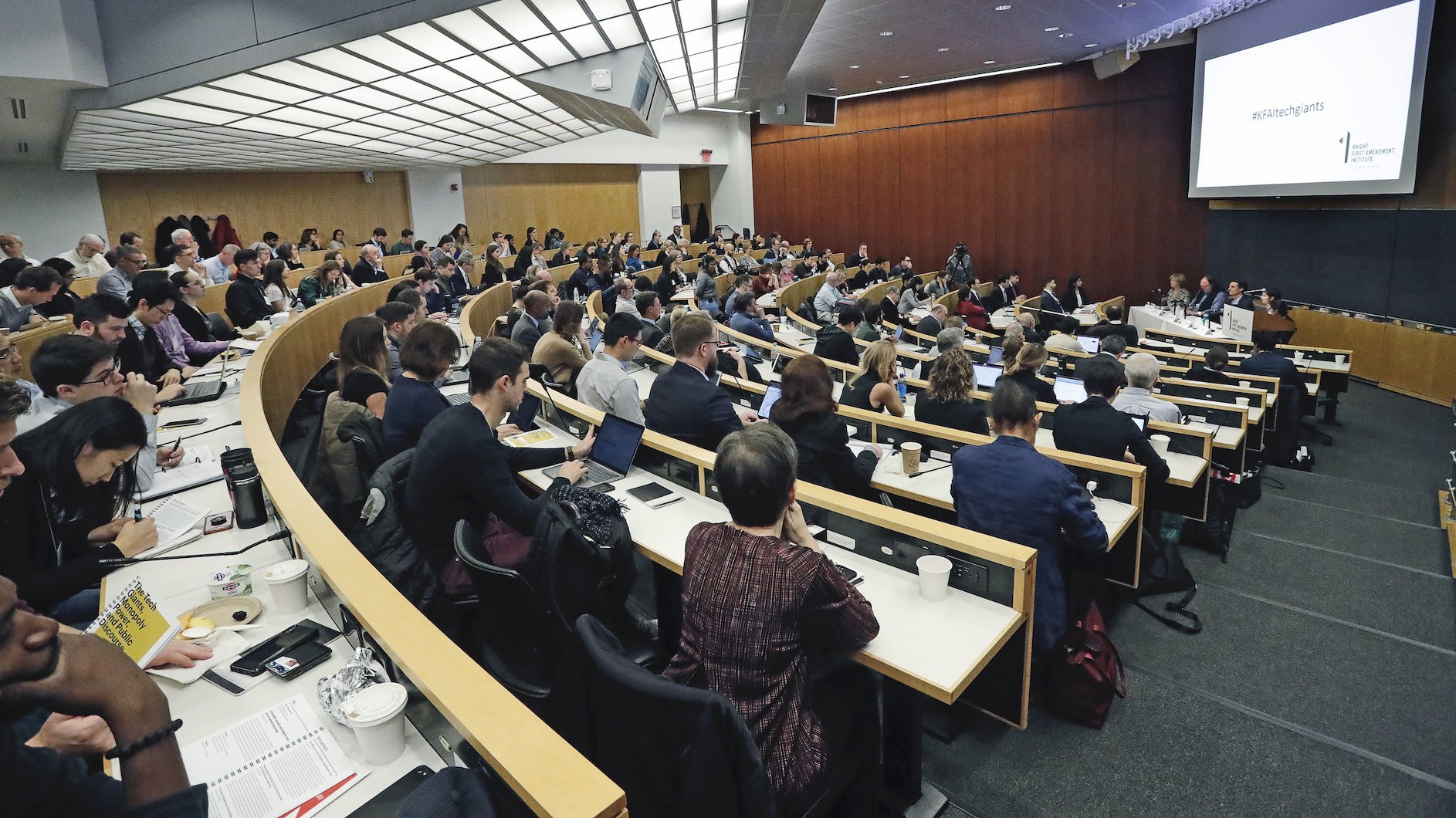 Audience of people watching a group of panelists speak in an auditorium