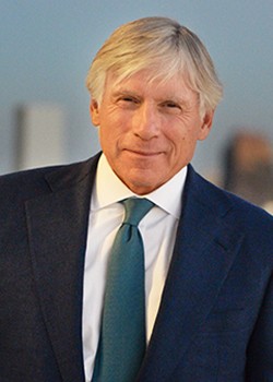 Light-skinned man with gray and white hair, in a dark suit