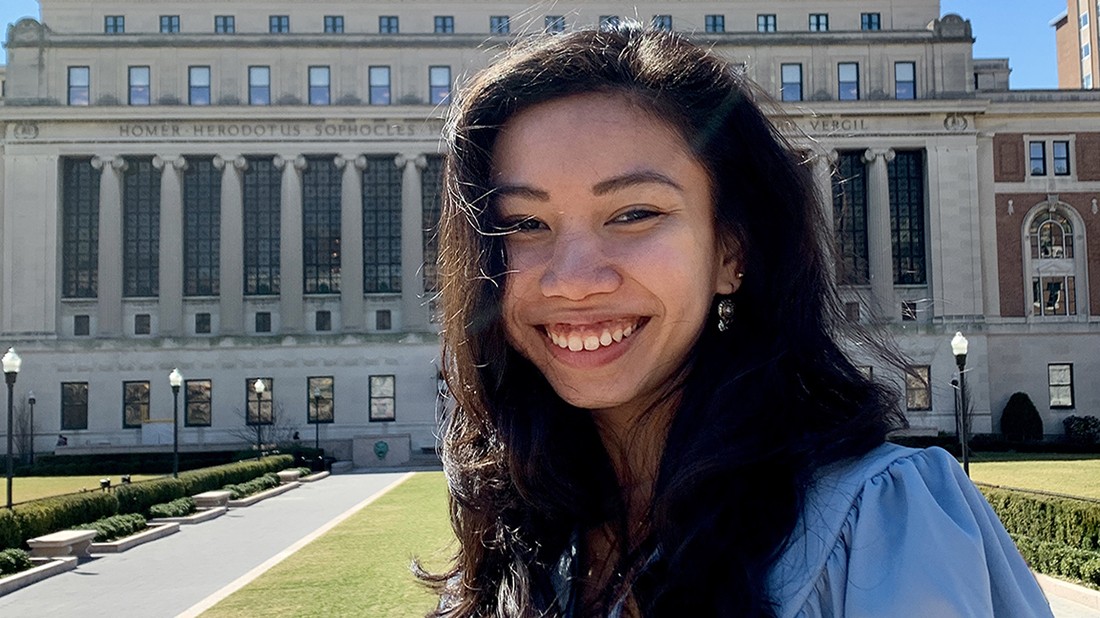 Jasmin Irisha Jim Ilham, on campus in mid-March, is a graduate student pursuing an MA in Climate and Society. A dark-haired woman in front of a columned building.