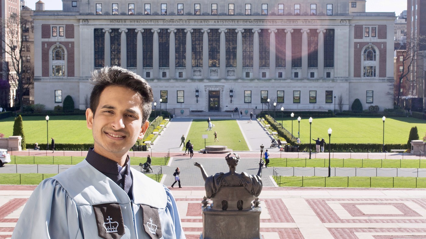 Sambhav Jain: A young man with dark hair wearing a graduation gown stands before a statue, lawn and big columned building.