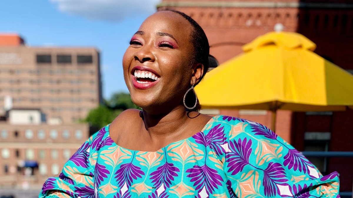 Tola Oniyangi: a smiling woman wearing a brightly colored shirt in front of a yellow umbrella.