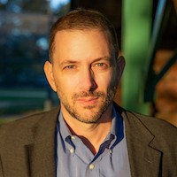 Adam Sobel: a headshot of a man with short brown hair who is wearing a blazer and a blue shirt