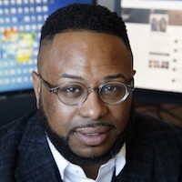 A headshot of a man with dark hair and wearing glasses